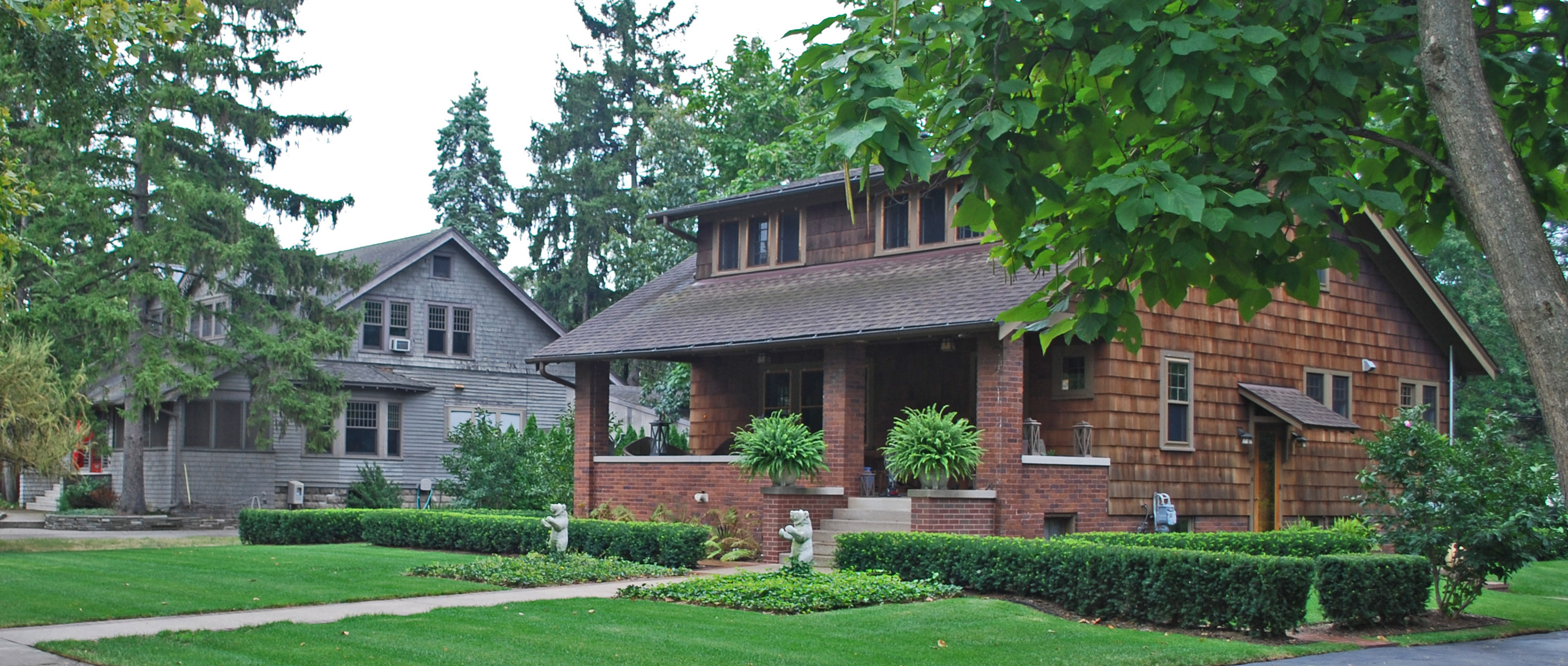 Green residential lawns and trimmed hedges in front of Craftsman homes in Pleasant Ridge near Ferndale